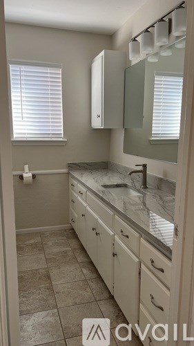 A bathroom with a marble countertop and white cabinets.