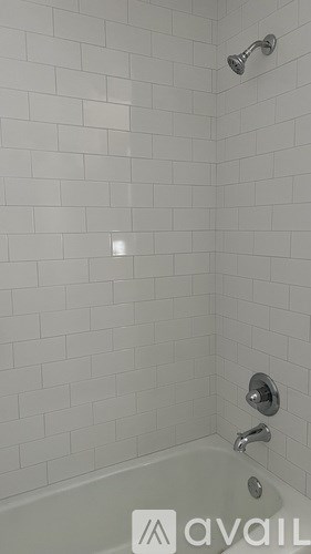 A white tiled shower with a faucet and a bathtub.