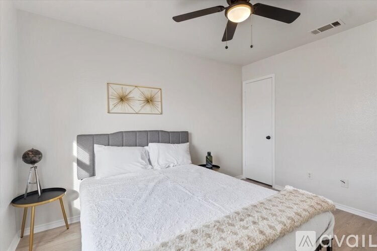 A bedroom with a bed, a ceiling fan, and a small table with a lamp on it.