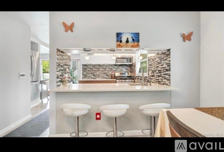 A kitchen with white stools and a stone backsplash.