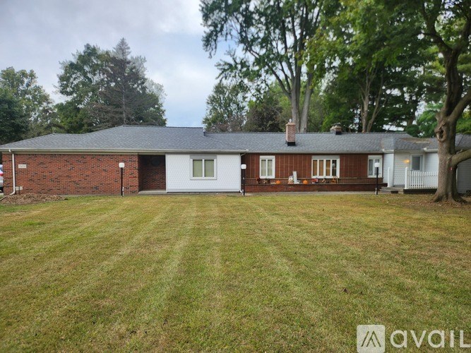 A house with a red brick exterior and a white door is surrounded by a grassy lawn.