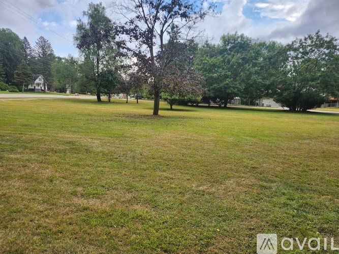 A grassy field with trees and a house in the background.