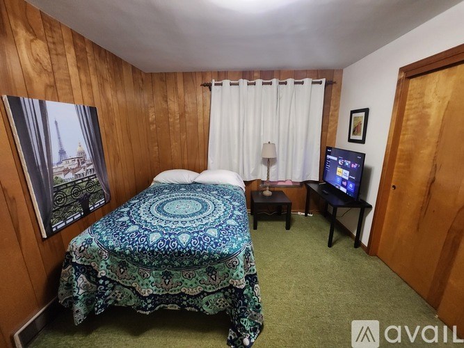 A bedroom with a bed, a small table, and a window with curtains.