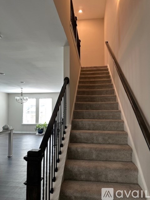 A staircase with a carpeted runner and black balusters leads up to a brightly lit landing.