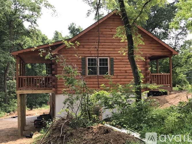 A wooden cabin with a porch is surrounded by trees and vegetation.