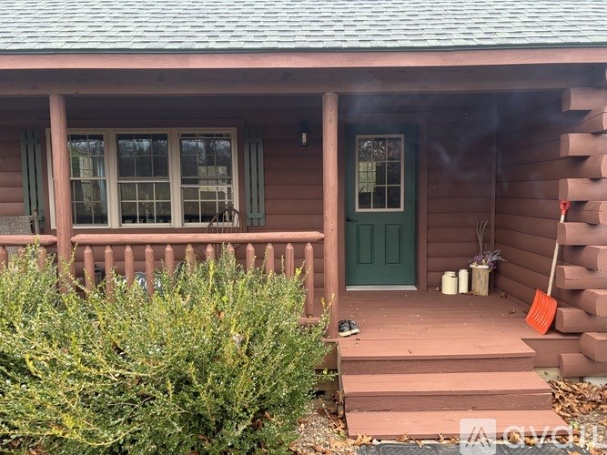 A small house with a green door and a red rake on the porch.