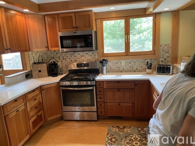 A woman is standing in a kitchen with wooden cabinets and stainless steel appliances.