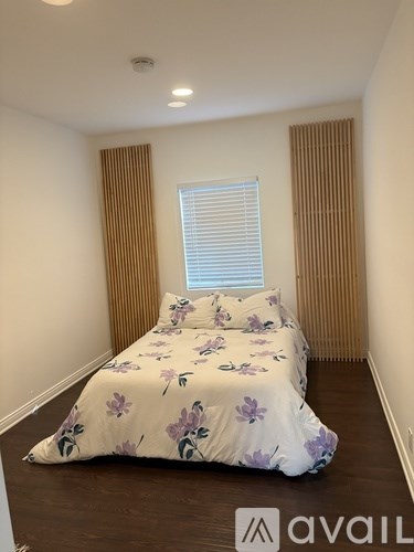 A bed with a floral comforter is in a room with a window and blinds.