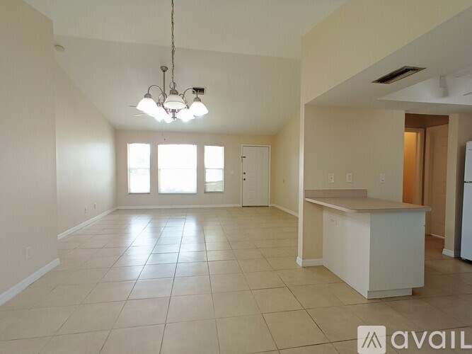 A large, empty room with a kitchenette and a chandelier.