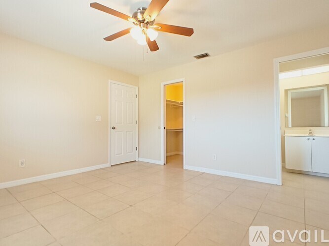 A spacious room with a ceiling fan and light fixture, tiled flooring, and a cabinet with a mirror.