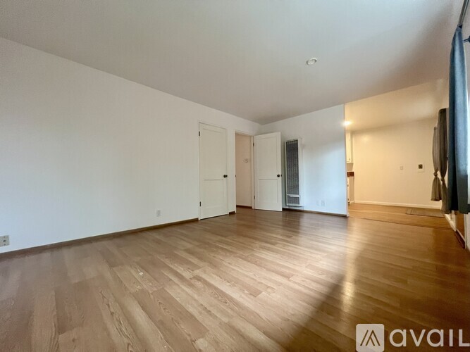 A spacious room with wooden flooring and white walls.