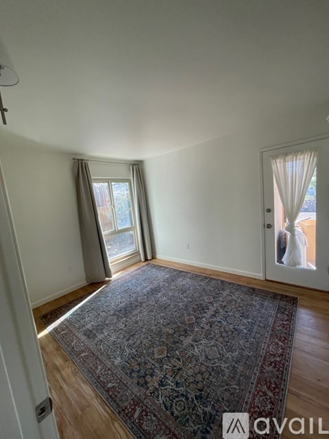 A room with a rug on the floor and a window with curtains.
