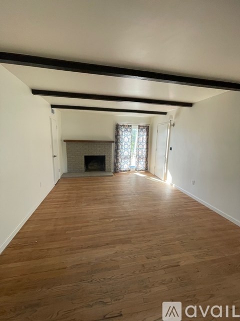 A room with wooden floors and white walls, with a fireplace and a window with curtains.