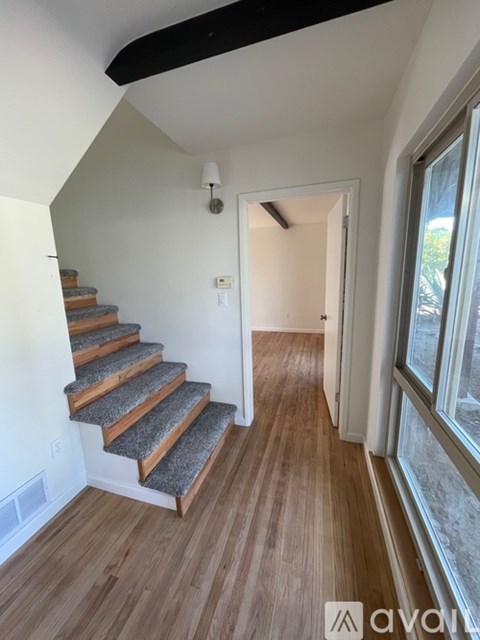A hallway with wooden floors and a staircase with a carpet runner.
