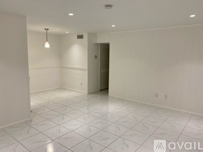 A spacious room with white tiled flooring and a single light fixture on the ceiling.
