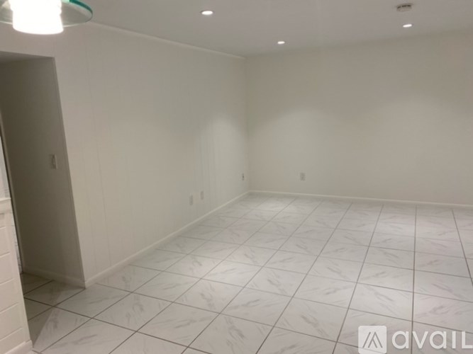 A room with white tiled flooring and walls, with a door on the left.
