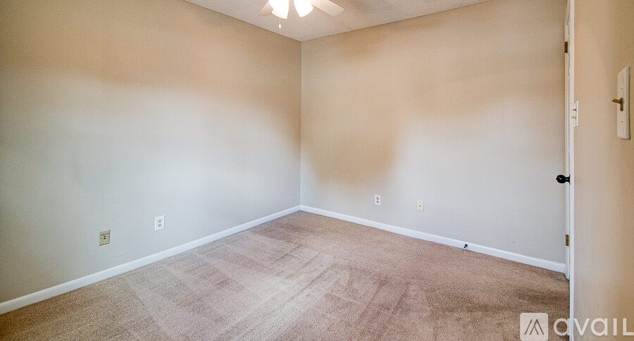 A room with beige carpet and walls, a ceiling fan, and a door.