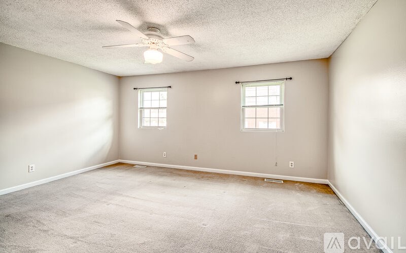A room with a ceiling fan and two windows.