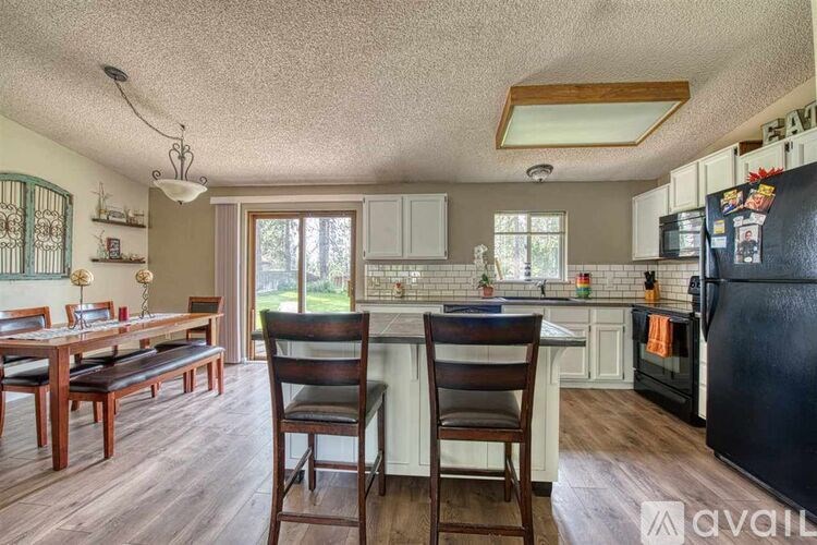 A kitchen with a black fridge and wooden chairs.