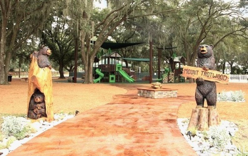 A pathway with a bear statue on the right and a tree stump on the left.