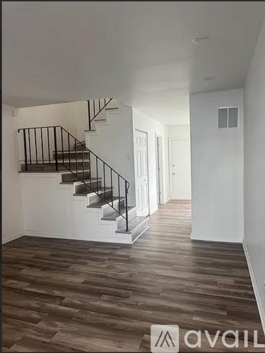 A wooden floor leads to a staircase in a white room.