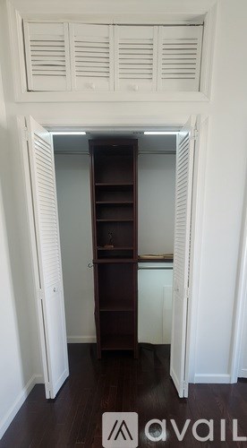 A small dark brown bookcase with four shelves is in a white room with a white ceiling fan.
