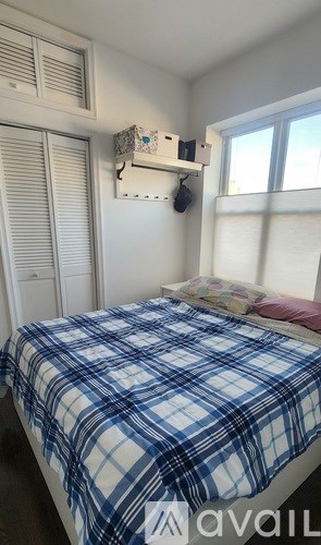 A bed with a blue and white plaid comforter sits in a room with a window and a white wall.