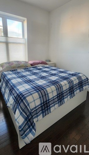 A bed with a blue and white checkered comforter is in a room with a window.