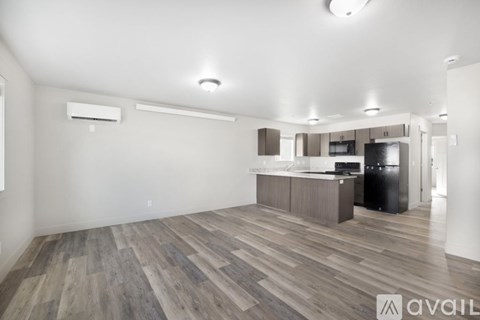 A spacious living room with wood flooring and a kitchen area in the background.