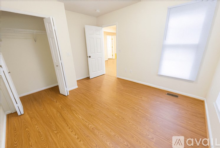A room with wooden flooring and white walls, with a door and a window.
