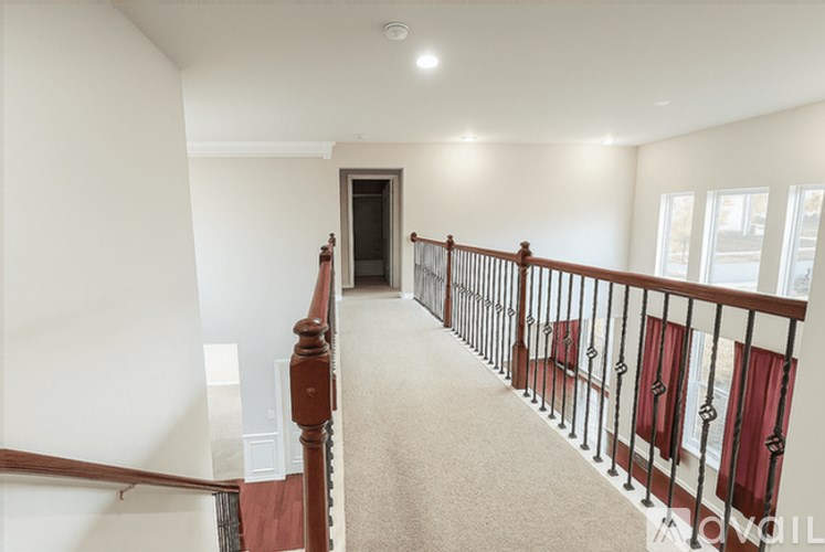A hallway with a carpeted floor, a wooden staircase with a metal railing, and a door at the end.
