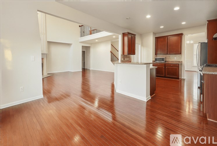 A spacious living room with hardwood floors and a kitchen area in the background.