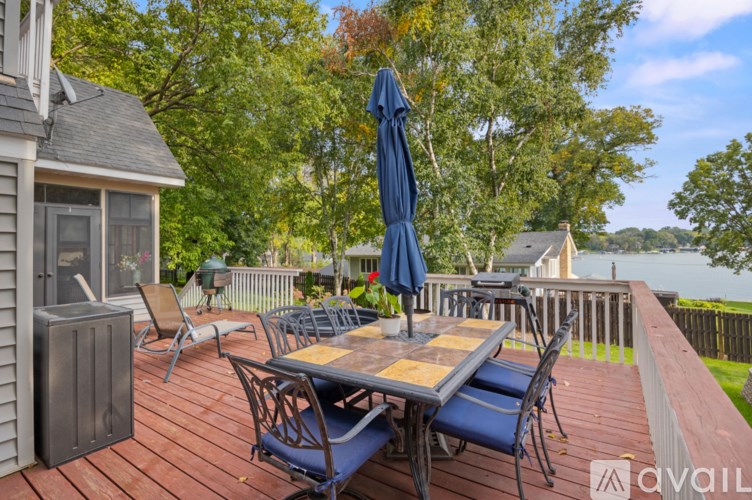 A wooden table with blue chairs and an umbrella on a deck overlooking a body of water.