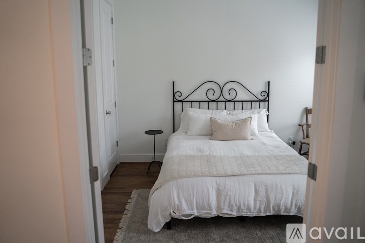 A bed with a white comforter and pillows sits in a room with a grey rug.