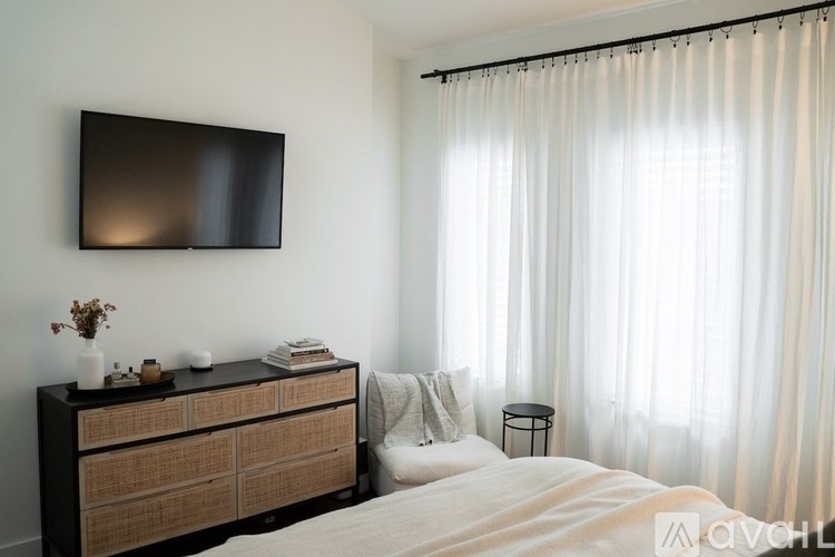 A modern bedroom with a large bed, a TV on the wall, and a wooden dresser with a vase of flowers on top.