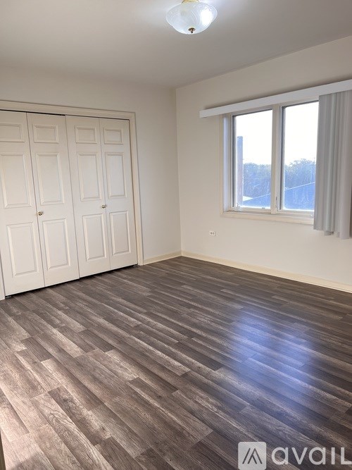 A room with wooden flooring and a window with white curtains.