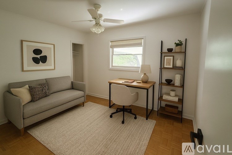 A living room with a grey couch, a desk with a chair, and a shelf with decorative items.