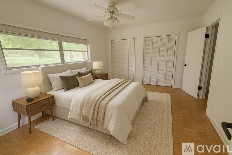 A bedroom with a large bed, a ceiling fan, and a window with blinds.