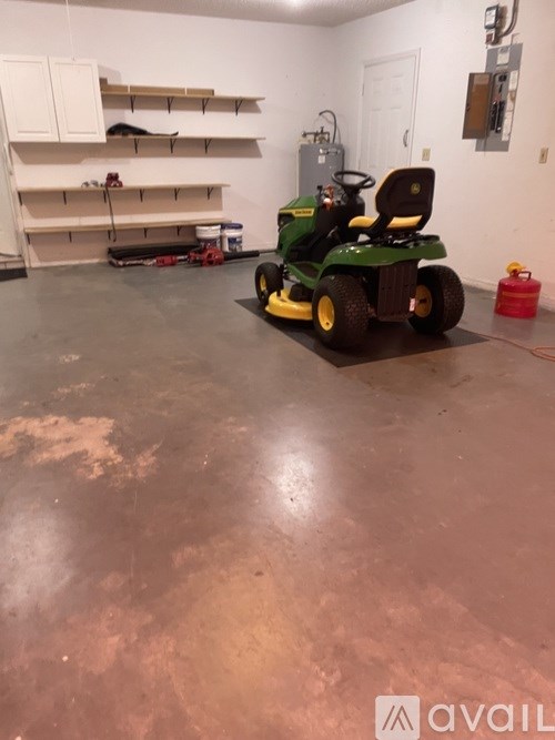 A green and yellow lawn mower is in a garage.