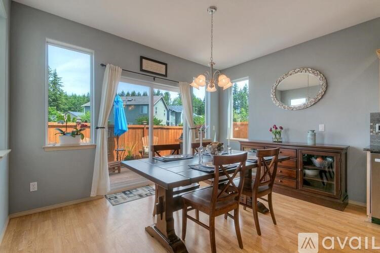 A dining room with a wooden table and chairs, a chandelier, and a view of a deck through the windows.
