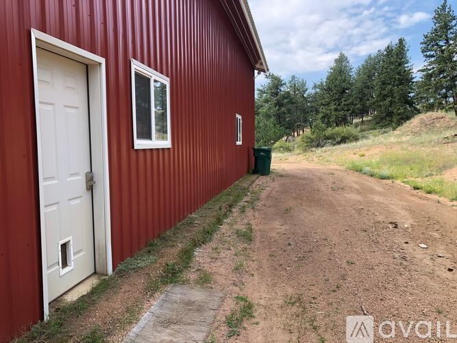 A red building with a white door and a small window is situated next to a dirt road.