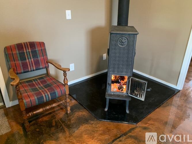 A wood stove is in a corner of a room with a plaid chair in front of it.