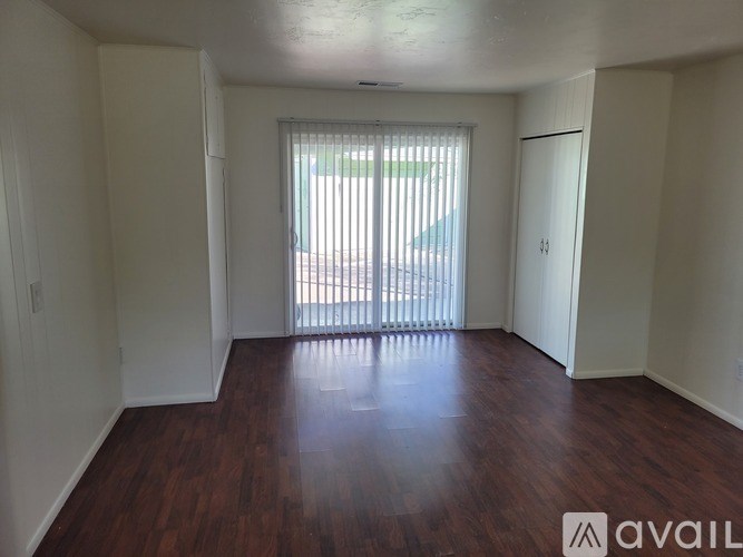 A room with wooden floors and white walls, with a window and sliding glass door.