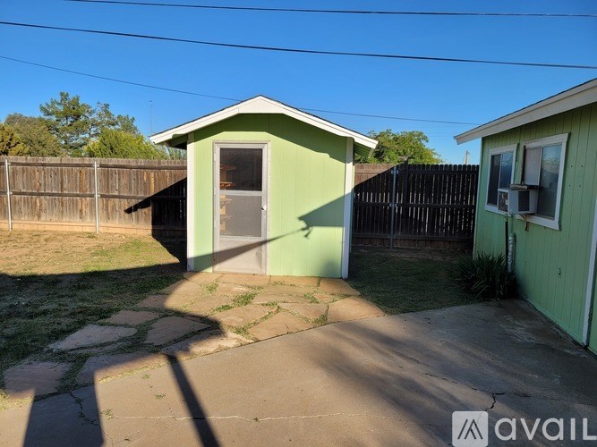 A green shed with a brown door is situated in a backyard.