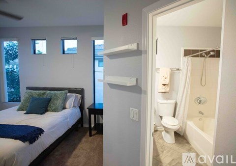 A bedroom with a bed, a nightstand, and a bathroom with a toilet and bathtub.