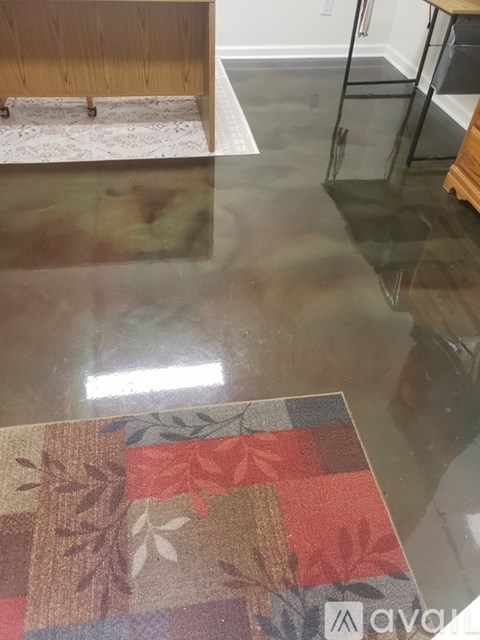 A table with a glass top reflects a room with a rug and a wooden bench.