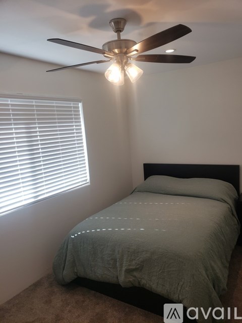 A bedroom with a bed, ceiling fan, and window with blinds.