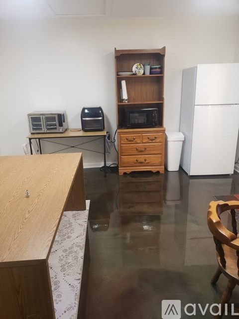 A kitchen with a wooden table, a microwave, a toaster, a printer, a refrigerator, and a wooden chair.