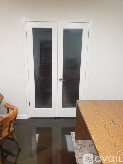 A white double door with a glass panel is in a room with a wooden table and a wooden chair.