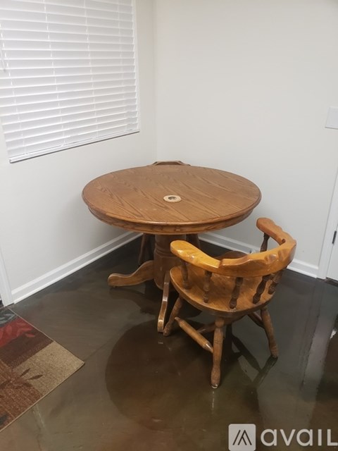 A wooden table and chair are in a room with a white wall and a window with blinds.